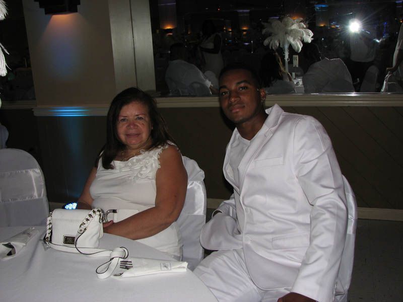 Woman and man seated at a white table. They are smiling, wearing white clothing, in a decorated room.