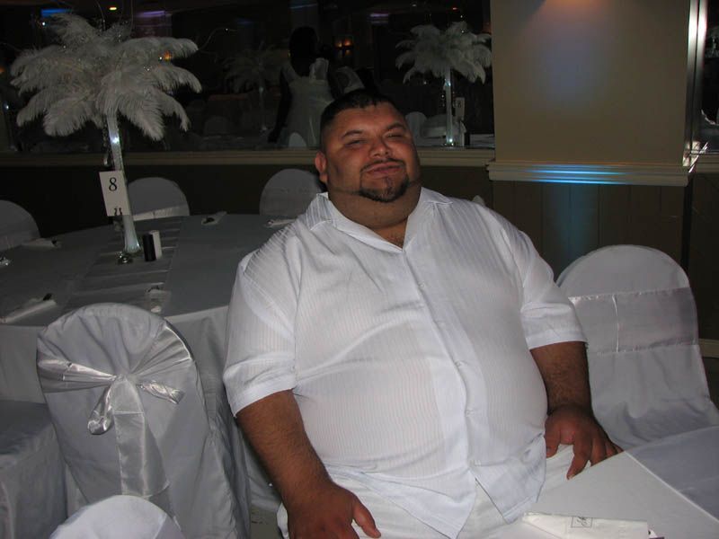 Man in white shirt seated at white table, formal setting.