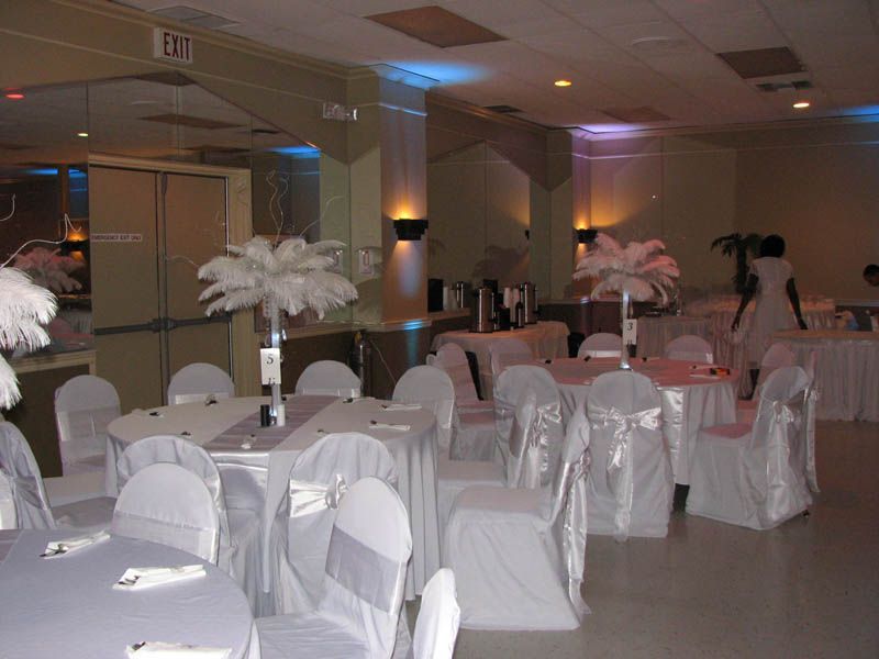 Formal event hall with round tables set for guests, adorned with white feather centerpieces.