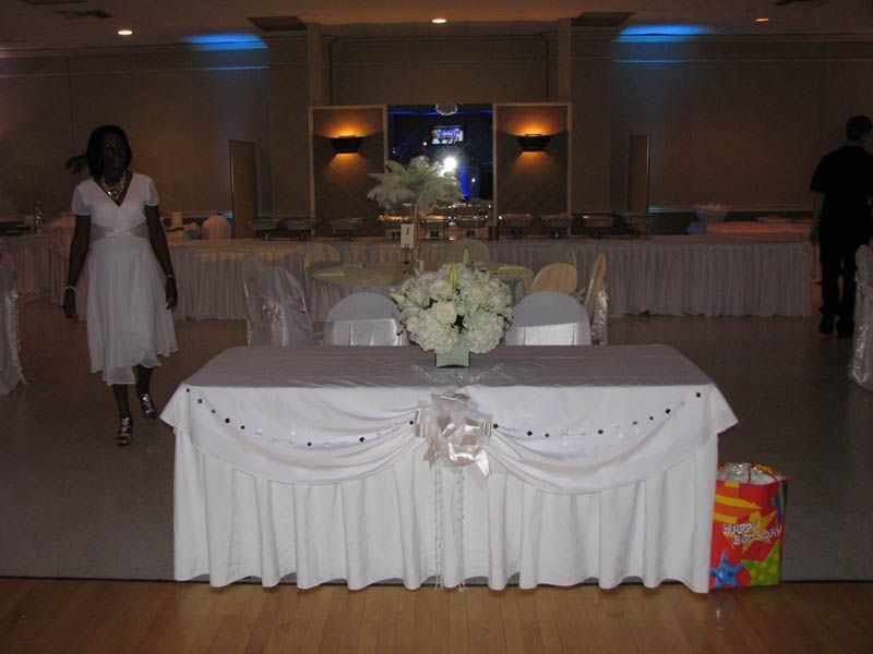Reception hall with a decorated table, flowers, and person walking.