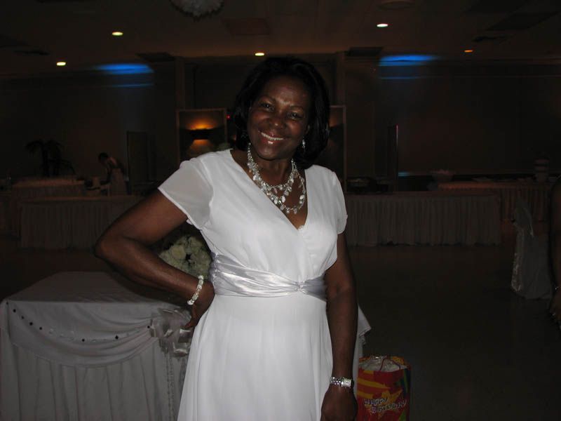 Woman in white dress smiles, poses in a decorated hall.
