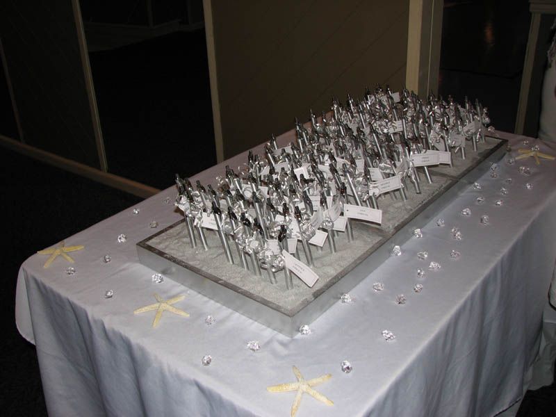 Table with silver forks, each holding a name card. White tablecloth with starfish and gems.