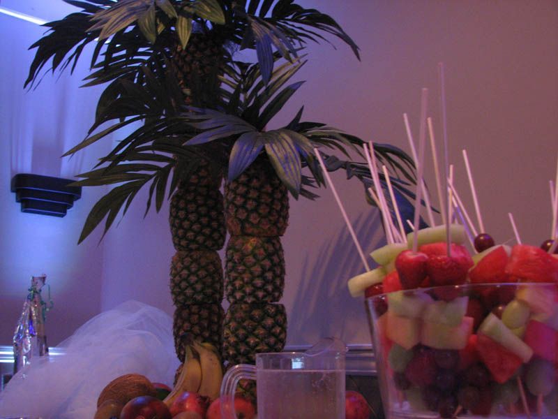 Fruit arrangement with pineapple palm trees and skewers of fruit in a clear glass bowl.