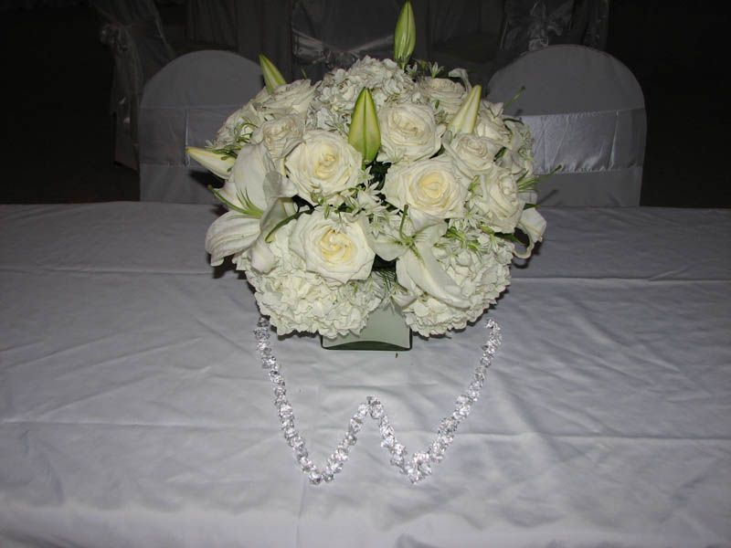 White floral arrangement centerpiece on a white tablecloth, with a beaded 