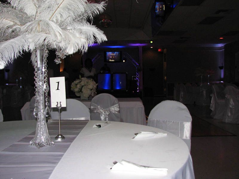 Formal dining room with white table settings, centerpieces, and stage with blue lights.