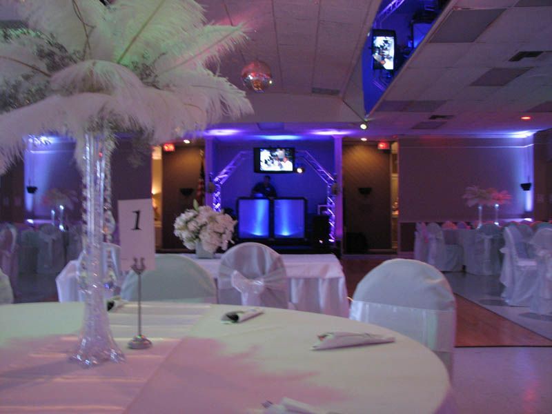 Reception hall with table settings and a DJ setup in the background, lit with purple and white lights.