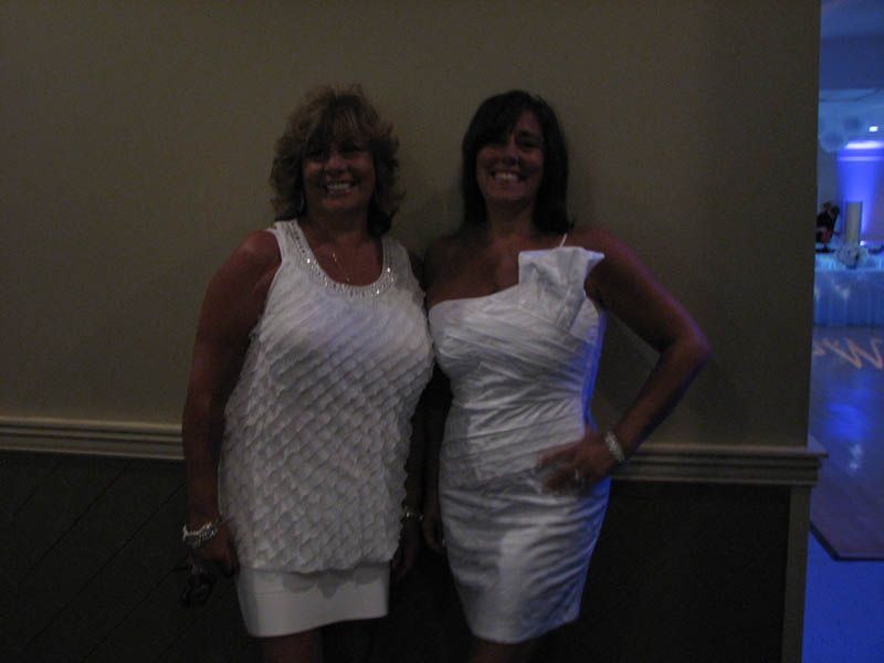 Two women in white dresses smiling in a room with blue lights in the background.