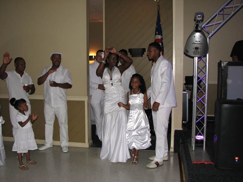 People in white formal attire dancing at an event, some waving.