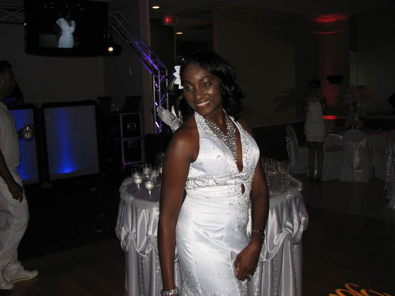 Woman in white dress smiles, posing at a party with tables and lights.