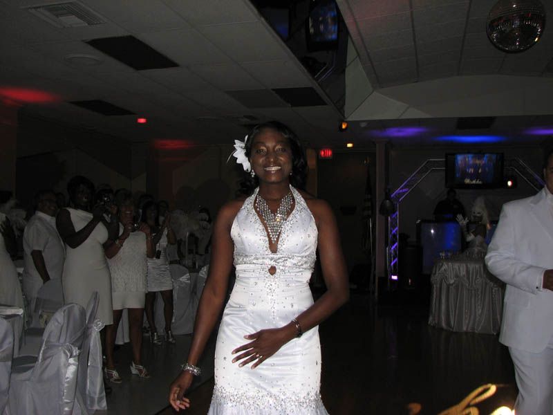 Woman in white wedding dress smiles, walks through reception hall. Guests in white clap.