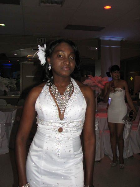 Woman in white gown, decorated with jewels, at a formal event. She has a flower in her hair.