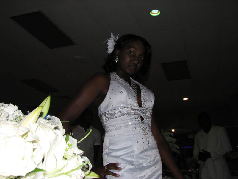 Woman in white dress, posing near flowers at an event, with dark setting.