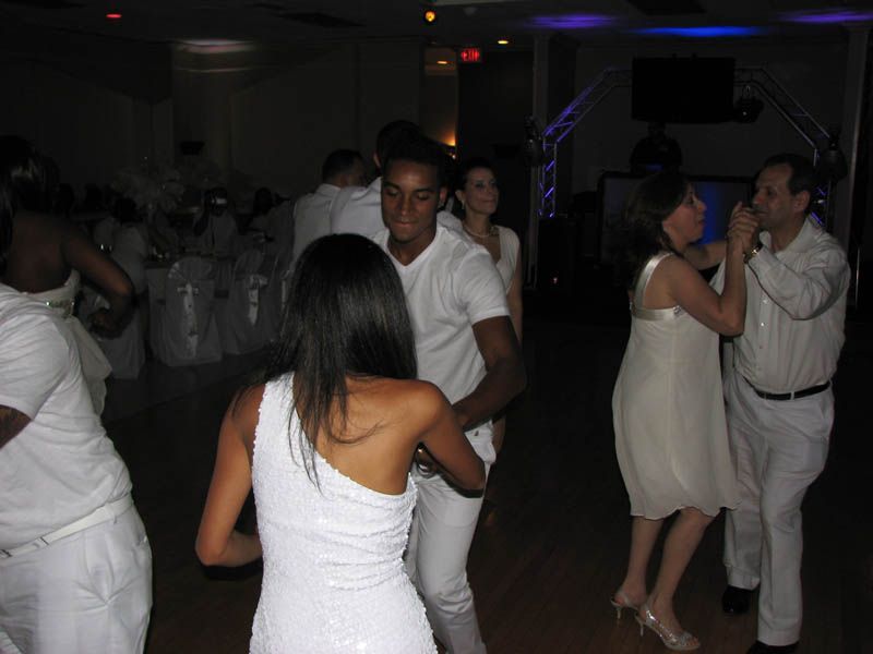 People dancing in a well-lit room; most wear white. Two couples face each other. Dim blue lights.