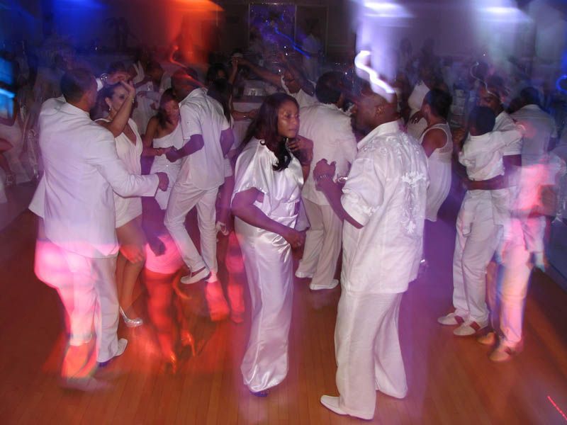 People dancing at a party, illuminated by colorful lights. All wear white clothing.