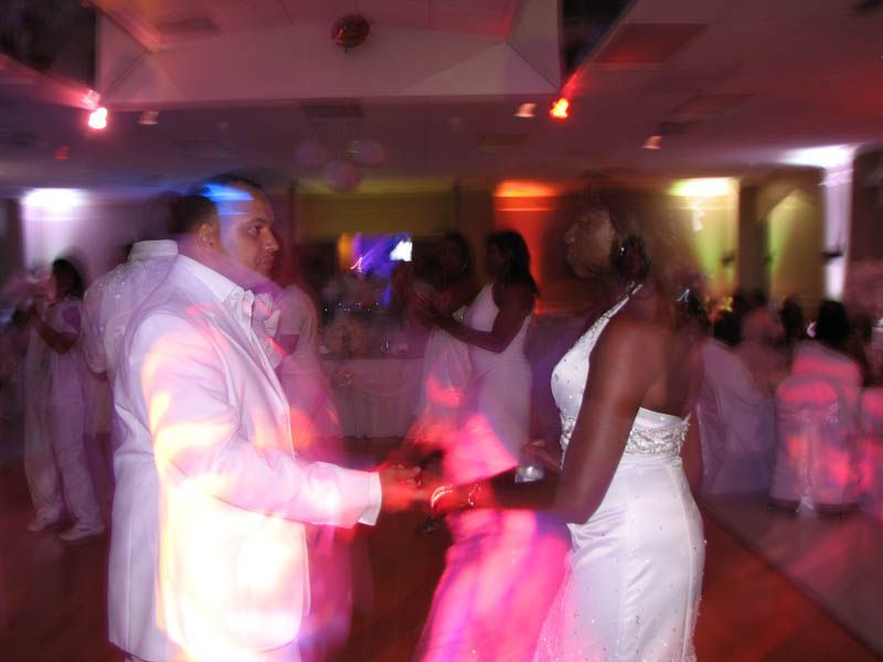 Couple dancing at a wedding reception, lit by colorful lights.