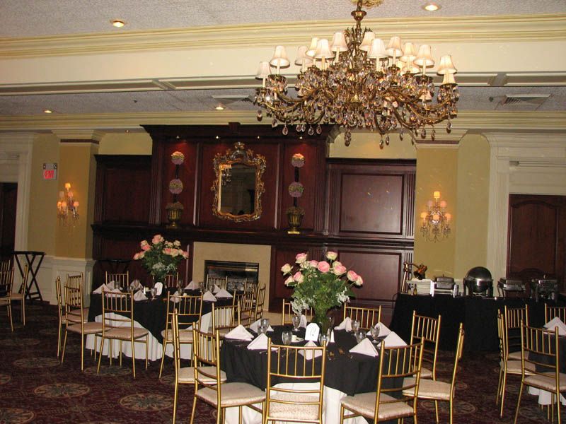 Formal dining room with tables set for a party, featuring a chandelier and fireplace.
