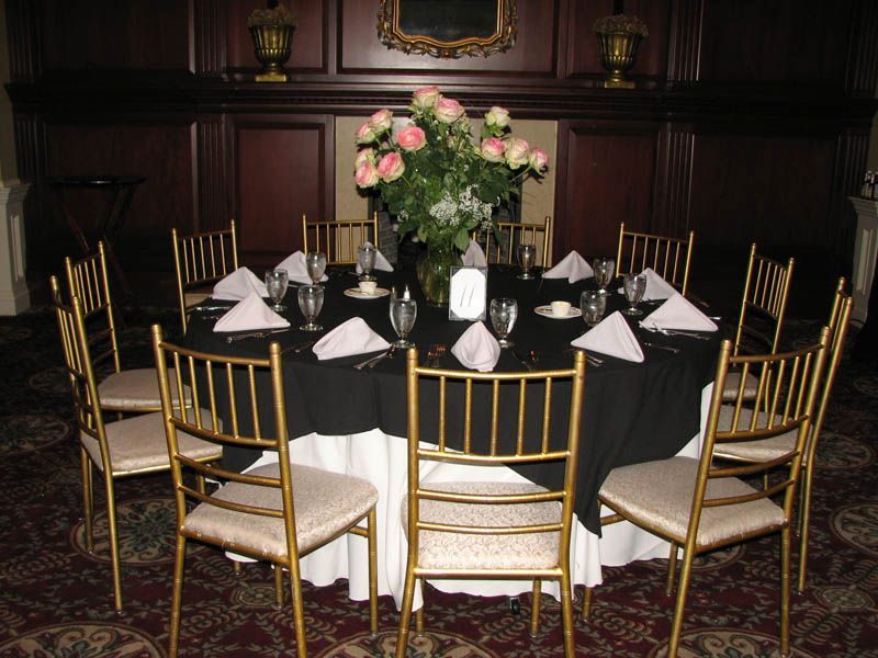 Round table set for a formal event with gold chairs, black tablecloth, white skirt, and a floral centerpiece.