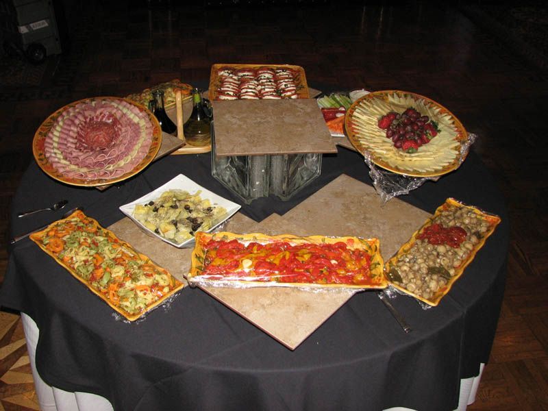 A table with various appetizers, including meat, cheese, tarts, and a vegetable display.