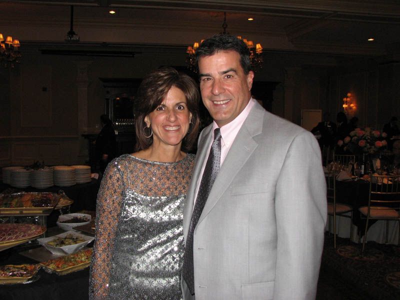 Woman in silver dress and man in gray suit pose together at an event.