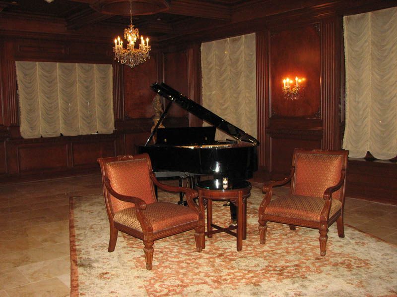 Elegant music room with grand piano, two armchairs, small table, chandelier, and sconces.