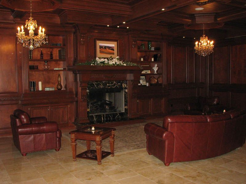 Elegant wood-paneled room with a fireplace, leather seating, chandeliers, and built-in shelving.