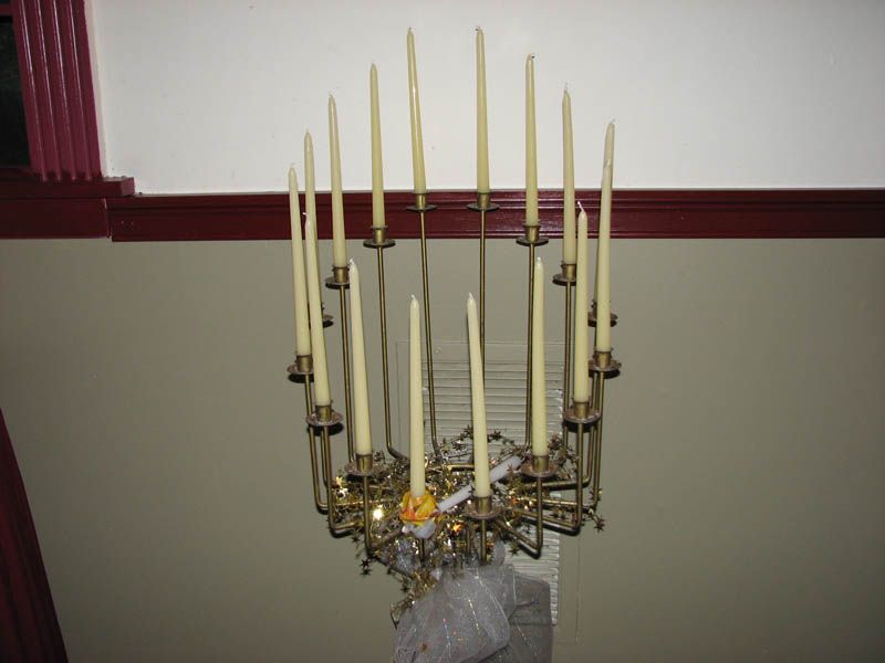 Candle chandelier hanging from a ceiling. Candles are lit. Beige walls.