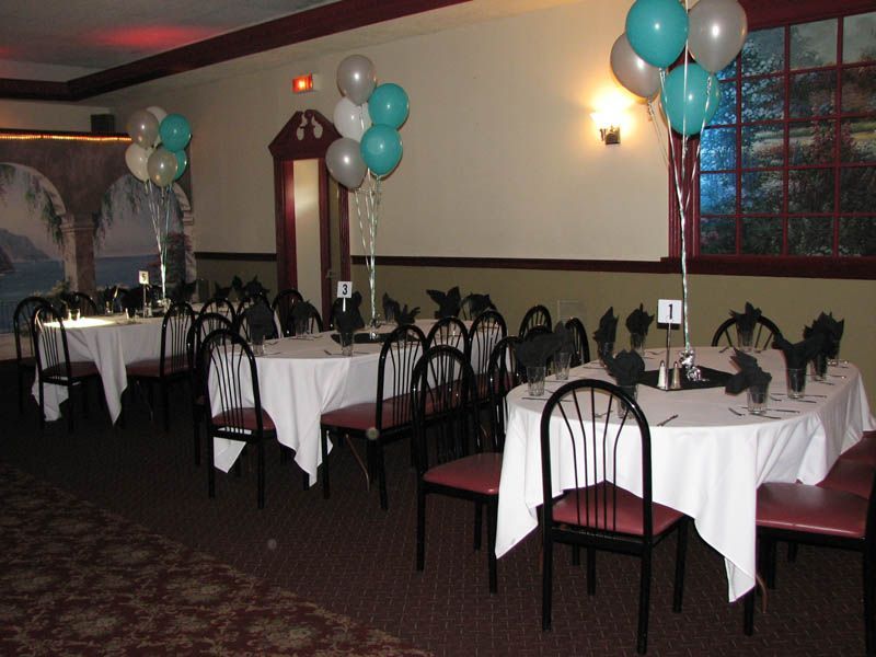 Tables set for an event with white tablecloths, black chairs, and teal and silver balloons.