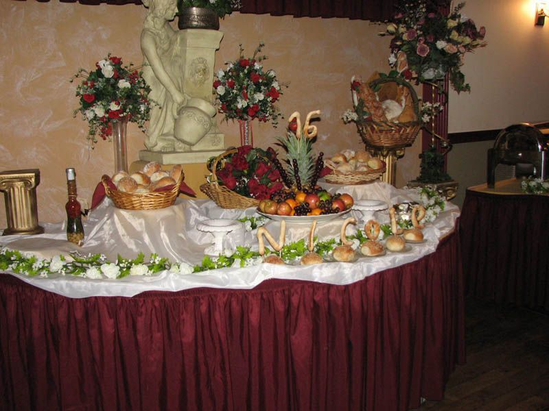 Buffet table with bread, fruit, and floral arrangements; red and white colors.