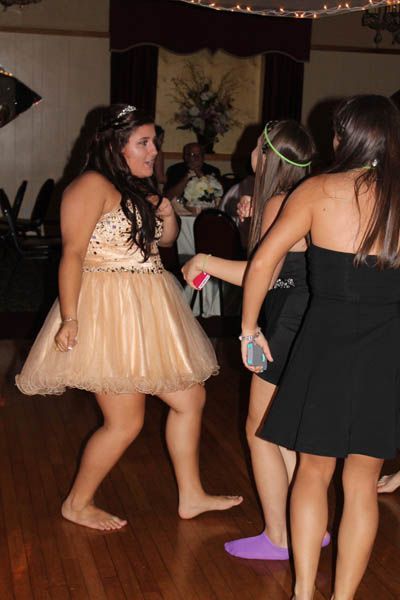 Three women dancing at an event, one barefoot in a short, tan dress, others in a black dress and another with a headband.