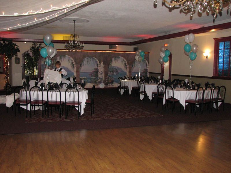 Banquet hall with tables set for a party, decorated with balloons and fabric.