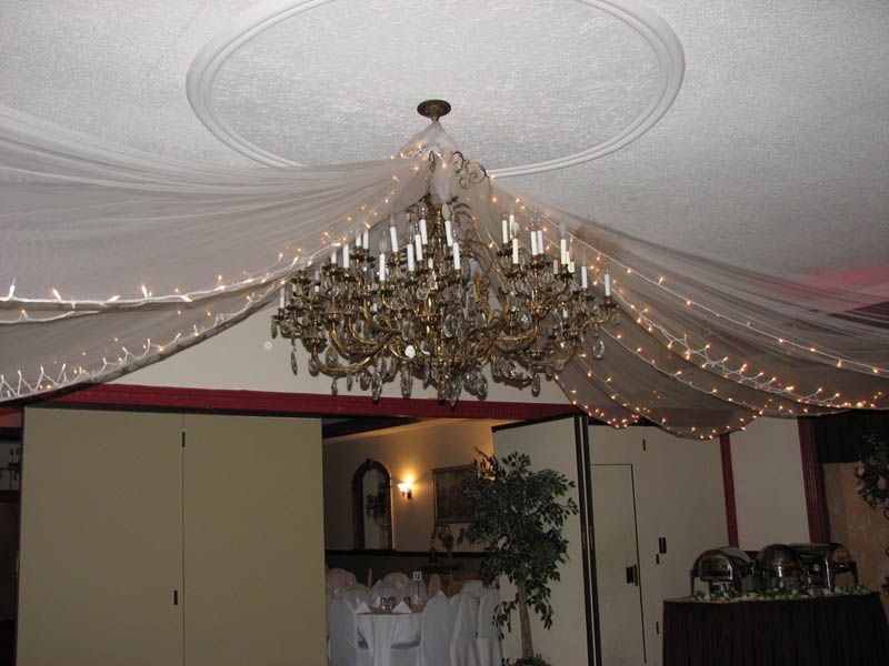 Chandelier in a room with draped fabric and string lights. Beige walls and a buffet are visible.