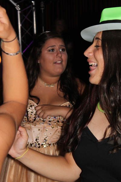 Two young women dancing at a party; one laughs, wearing a hat, the other watches.