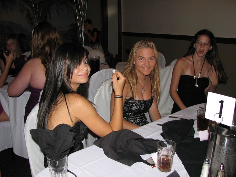 Three women at a table wearing formal dresses, smiling at a social gathering. Black and white table settings.