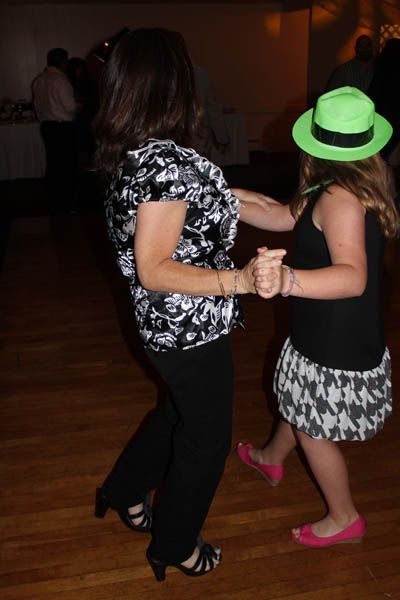 Woman and child dancing on a wooden floor; child wears a green hat and black and white skirt.
