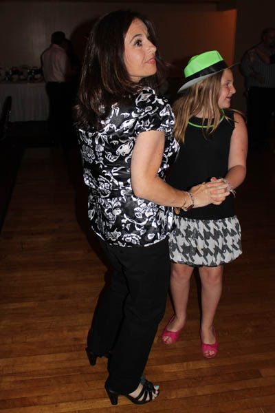 Woman dancing with person wearing a green hat and houndstooth skirt at an event.