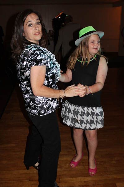 Woman and girl dance, woman in black and white blouse, girl in black and white skirt and neon hat, party setting.