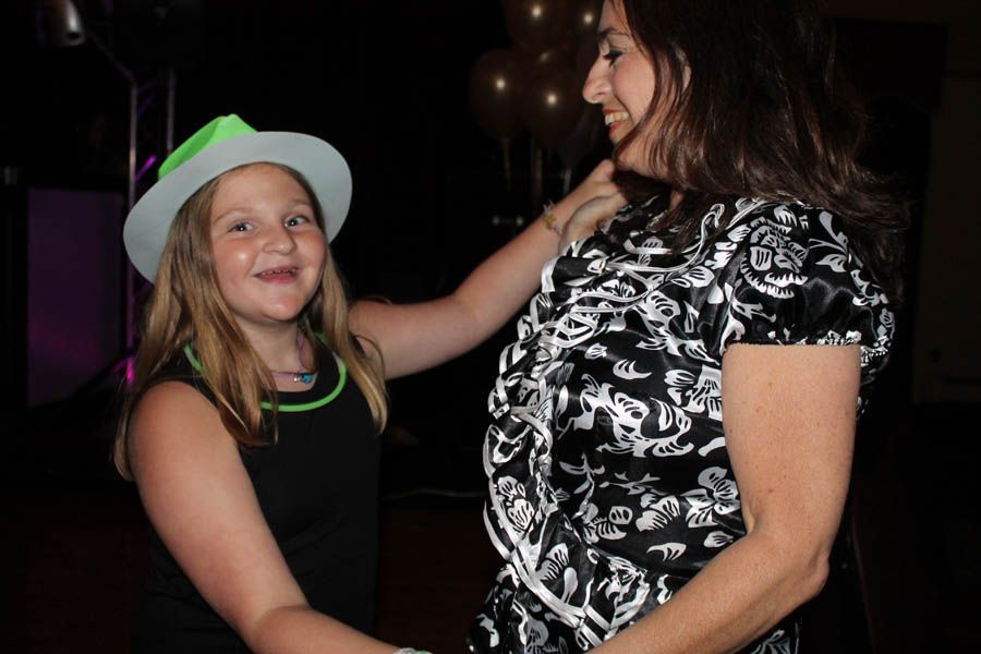 Girl in neon hat and necklace dancing with a woman in a black and white floral top.