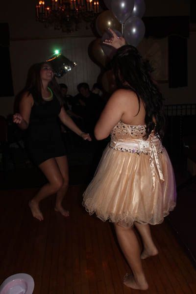 Two people dancing barefoot at a party with balloons. One wears a short, peach dress.