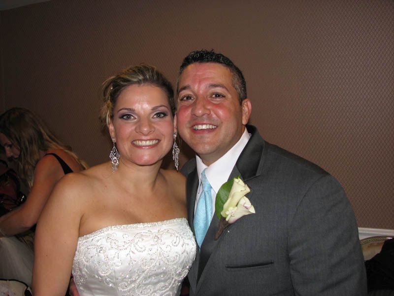 Bride and groom smiling at a wedding reception. Woman in a white strapless dress, man in a gray suit with a teal tie.