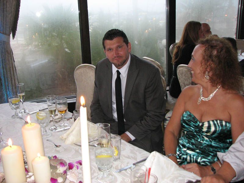 Man in a suit sits at a table with a woman in a green dress. Candles and glasses on the table.