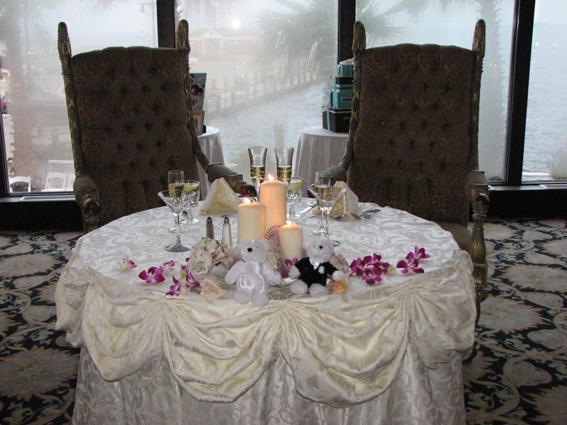 Wedding table set with champagne, candles, and decorations, flanked by ornate chairs, indoors.