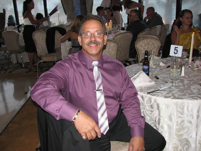 Man in purple shirt, striped tie, seated at a table in a banquet hall.