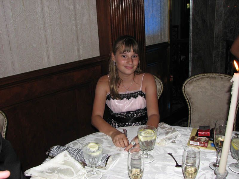 Girl in a pink and black dress sits at a table with glasses and candles.