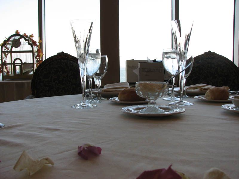 Table set for a meal with tall champagne flutes, plates, and rolls, by a large window.