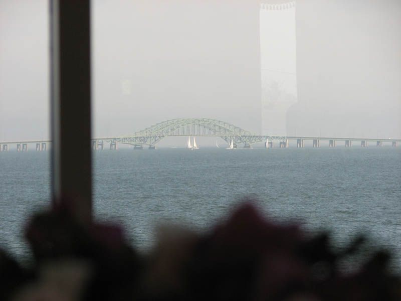 Bridge over water with sailboats, seen through a window. Overcast sky.