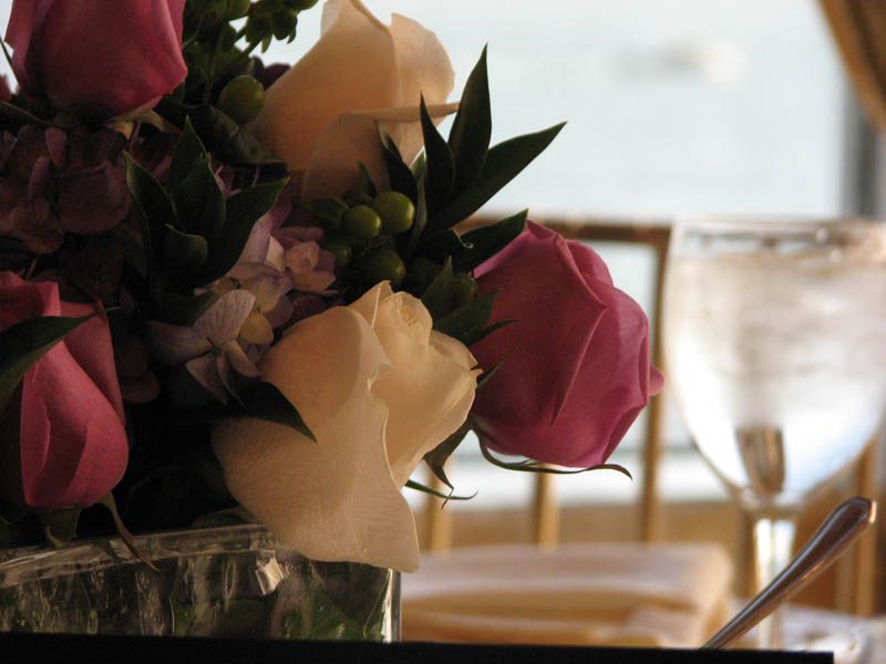 Bouquet of pink and cream roses on a table, next to a water glass.