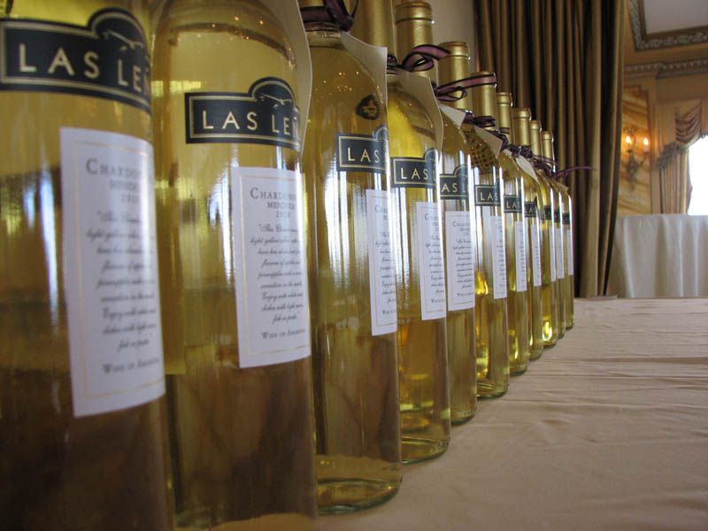 Row of wine bottles with golden liquid on a table, partially visible labels, indoor setting.
