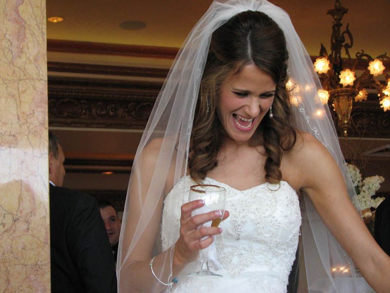 Bride in white dress, veil, laughing, holding drink at wedding reception.