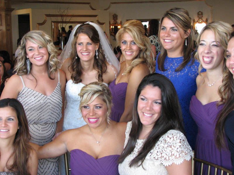 Group of women smiling at a wedding. Bride in white dress, bridesmaids in various purple dresses.
