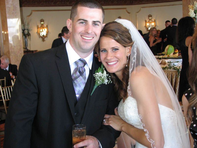 Bride and groom smiling at a wedding, he holds a drink, indoors.